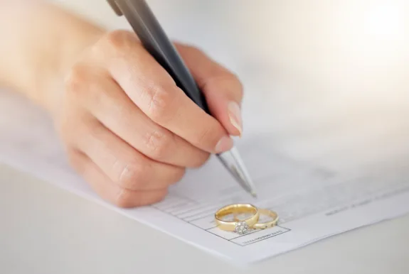 Person writing signature on marriage paperwork after agreement at family law office