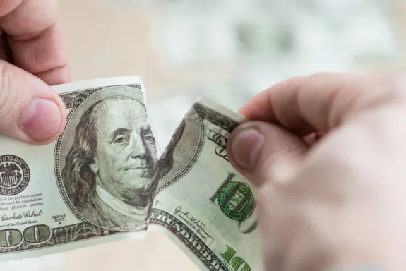 Two hands tearing hundred dollar bill